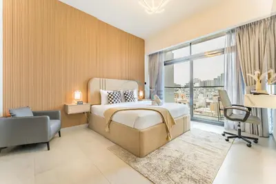 a bedroom with a bed and a desk and a window at Community View 1BR, Just 15minutes to Miracle Garden - Oxford Boulevard, Jumeirah Village Circle by Deluxe Holiday Homes in Dubai