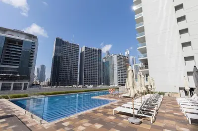a pool with lounge chairs and umbrellas in a city at 1BR Facing Canal and City Views, Just a Short Walk to Bus Stop and Marine Transport, Reva Residences, Business Bay by Deluxe Holiday Homes in Dubai