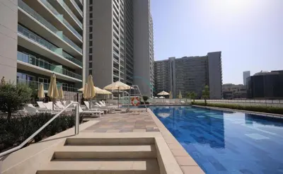 a swimming pool with chairs and umbrellas next to a building at 1BR Facing Canal and City Views, Just a Short Walk to Bus Stop and Marine Transport, Reva Residences, Business Bay by Deluxe Holiday Homes in Dubai