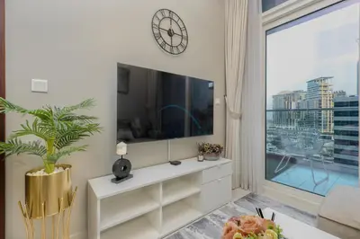 a living room with a tv and a large window at 1BR Facing Canal and City Views, Just a Short Walk to Bus Stop and Marine Transport, Reva Residences, Business Bay by Deluxe Holiday Homes in Dubai
