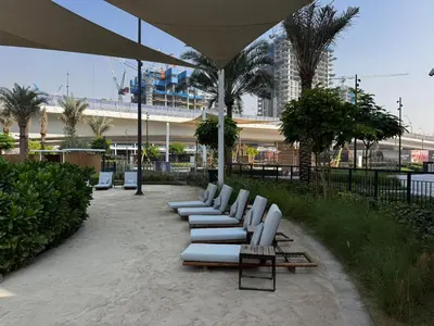 a row of white lounge chairs and an umbrella at Elegant 1BR at Lotus Creek Beach Lagoon Living in Dubai