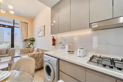 a kitchen with a stove top oven next to a living room at Elegant 2BR Getaway in Azizi Riviera Near Downtown in Dubai