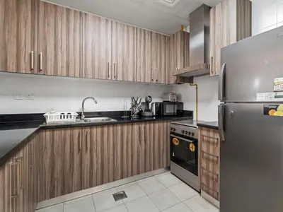 a kitchen with wooden cabinets and a stainless steel refrigerator at Urban Elegance 1BDR in Dunya 06 in Dubai