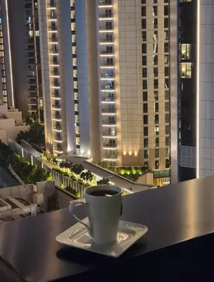 a cup of coffee sitting on a table with a view of buildings at Damac Maison Mall Street LARGE 2BR I Full Burj Views I Connects Dubai Mall in Dubai