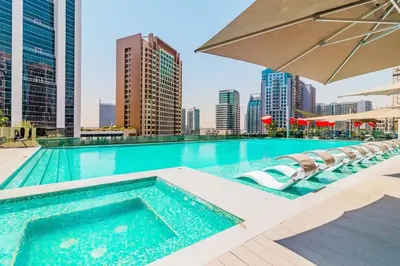 a swimming pool with chairs and an umbrella on a building at Vogue Downtown Mag 318 near Burj Khalifa and Dubai Mall, Studio Apartment with Balcony, Canal and City Skyline View, Access to all Amenities in Dubai