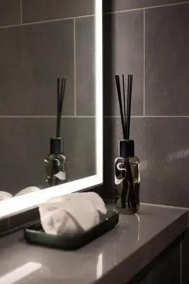 a bathroom counter with a mirror and two vases with sticks at Cosy Sobha Hartland Apt - Pool&Gym - Near Downtown in Dubai