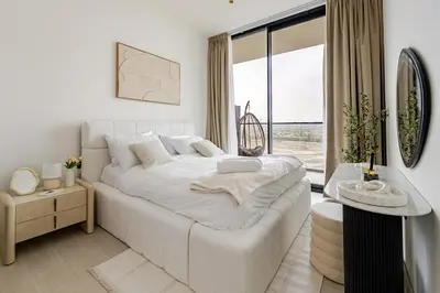 a white bedroom with a large white bed and a window at Cozy and Stylish 1BR in JVC in Dubai