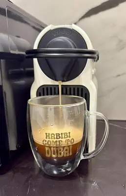 a coffee maker is pouring coffee into a glass cup at Stylish central apartment, own Jaccuzi, burj view in Dubai