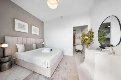 a white bedroom with a bed and a mirror at StayShort - Chic studio in Production City that sleeps 4 in Dubai