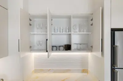 a kitchen with white cabinets with glassware at Upscale 4BR Loft Duplex plus Maid in Creekside, Creek Harbour in Dubai