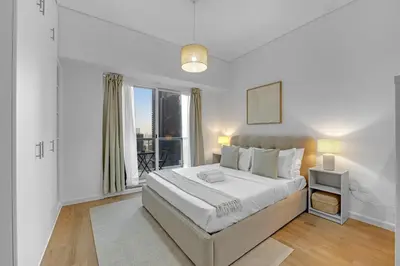 a white bedroom with a large bed and a window at Waves - Modern Lakeview Studio - Cozy & Bright in Dubai