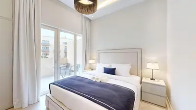 a white bedroom with a large bed and a balcony at Vacationer l Modern Aesthetic 1 Bed l JVC l near Circle Mall in Dubai