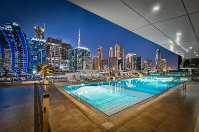 a large swimming pool with a city skyline at night at Modern 1BR Apartment - Burj Khalifa View - Pool & Terrace - Near Metro in Dubai