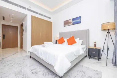 a white bedroom with a large bed with orange pillows at Bright Studio with Pool Access - Azizi Riviera in Dubai