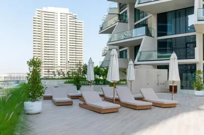 a patio with lounge chairs and umbrellas in front of a building at Luxury 1BR Apartment with Private Pool & Gym Access in Dubai