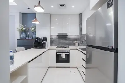 a kitchen with white cabinets and a stainless steel refrigerator at Modern Chic 1BHK Nobles Tower by Czechin in Dubai