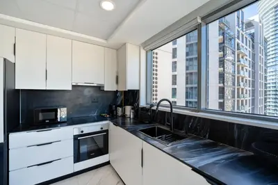 a kitchen with white cabinets and a large window at Marcopolo - Signature High-Floor Apartment Facing Burj Khalifa in Sabkhah