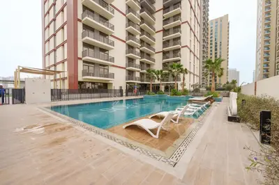 a swimming pool with lounge chairs and a building at Calm & Stylish 1Bedroom in Hadley Heights JVC in Dubai