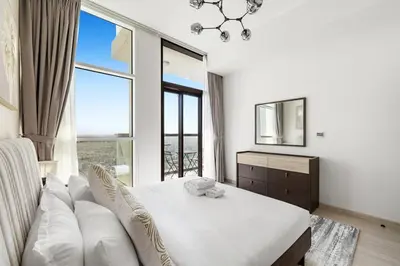 a white bedroom with a couch and a large window at Cozy 1BR Near Metro in Starz Tower 2 in Dubai