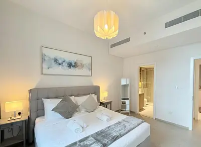 a bedroom with a bed with white sheets and a chandelier at Cozy & Stylish 1BR in Wilton Terraces in Dubai