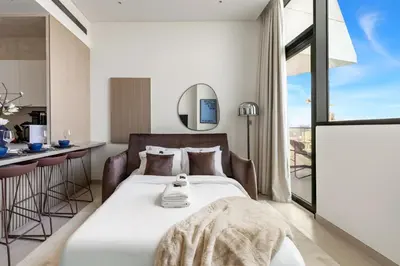 a bedroom with a bed and a table and a kitchen at Stylish 1BR with Private Pool Near Circle Mall in Dubai