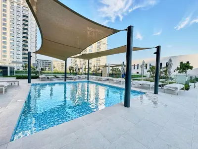 a swimming pool with a large umbrella on a building at Luxury 1BR Apartment Steps from Dubai Hills Mall in Dubai