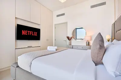 a white bedroom with a bed and a tv at Luxury 1BR Apartment Steps from Dubai Hills Mall in Dubai