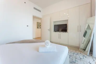 a white bedroom with a bed and a tv at Stylish 2BHK with Burj Khalifa Views in Downtown in Dubai