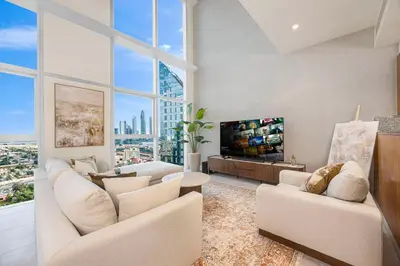 a living room with white furniture and a large window at Daniels 2BR Duplex at Central Park Tower, DIFC in Dubai