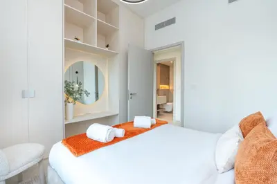 a white bedroom with a bed and a chair at PVH - Chic Pool View 2BR Near Dubai Hills Park - Park Field Tower 2 in Dubai