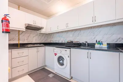 a white kitchen with a washing machine in it at Family-Friendly Apartment, Few Minutes Drive to Dubai Marina, Miracle Garden and Mall of the Emirates - Elite Residences 4, Sports City by Deluxe Holiday Homes in Dubai