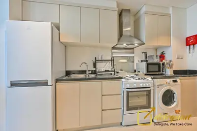 a kitchen with white cabinets and a sink and a refrigerator at Modern Comfort Studio DAMAC Hills 1 in Dubai