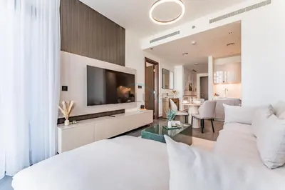 a bedroom with a white bed and a living room at Prime 1BR, Few minutes Drive to Burj Khalifa and Dubai Mall - Sobha Hartland The Crest Tower C by Deluxe Holiday Homes in Dubai