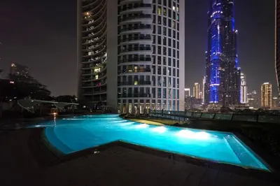 a large swimming pool in a city at night at Paradise Retreats 3BR Burj Khalifa & Fountain view in Dubai