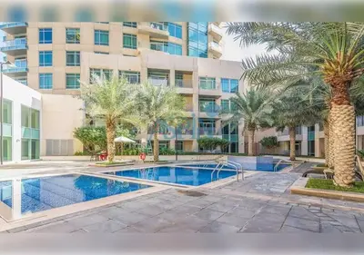a swimming pool with palm trees and a building at Aspin Brand New Premium Studio with Pool View - Burj Views in Dubai