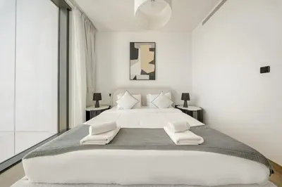 a white bedroom with a large bed with two tables at VayK - Stylish 2BR & Maids Apartment in Sobha Hartland in Dubai