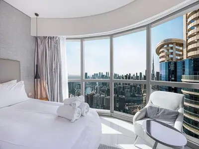 a bedroom with a bed and a chair and a large window at Spacious 3BR in Paramount Tower Luxury Living in Dubai