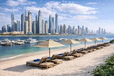 a beach with chairs and umbrellas in front of a city at Elegant Beachfront 2BR at Palace Beach Residence in Dubai