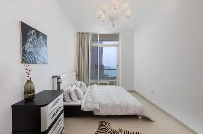 a white bedroom with a bed and a chandelier at VayK - Amazing 1BR in Marina with Sea View in Dubai
