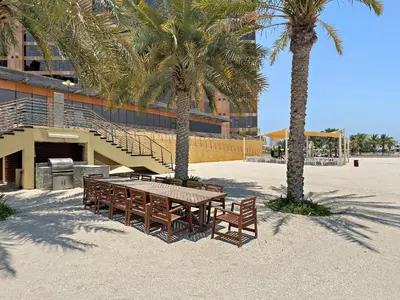 a picnic table and two palm trees in front of a building at VayK - Spacious 2BR with Private Gym & Beach Access in Dubai