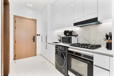 a white kitchen with a stove and a microwave at ALiving Cozy Studio I Binghatti Galaxy, JVC- G02 in Dubai