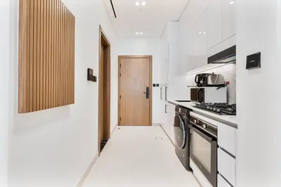 a kitchen with white walls and a wooden door at ALiving Cozy Studio I Binghatti Galaxy, JVC- G02 in Dubai