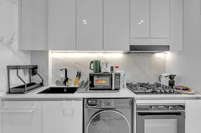 a white kitchen with a stove and a microwave at Charming Studio in Binghatti Galaxy JVC in Dubai