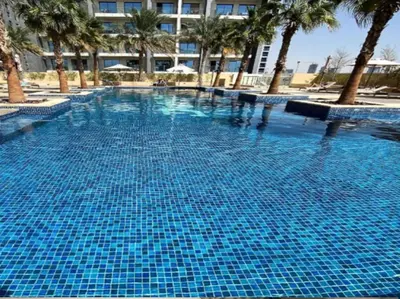 a large blue swimming pool with palm trees and a building at Glamorous Luxe Studio in Ghalia-JVC-12 in Dubai