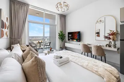 a white bedroom with a large bed and a table at Cozy Studio with 31st Floor Miracle Garden View in Dubai