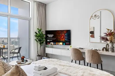 a white room with a bed and a table with chairs at Cozy Studio with 31st Floor Miracle Garden View in Dubai