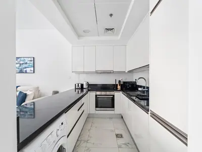 a white kitchen with white cabinets and black counter tops at Charming City View w 1BDR Apartment In Noura Tower in Dubai