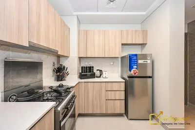 a kitchen with wooden cabinets and a stainless steel refrigerator at Oversized 1BR Apartment Near Dubai Hills Mall in Dubai
