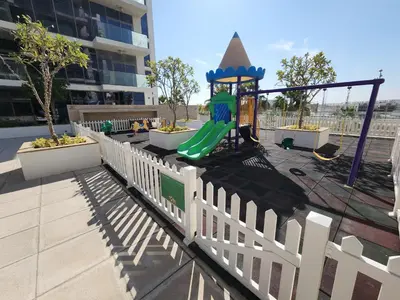 a playground with a green slide and a white fence at Spacious Golf & Pool View Home with Huge Balcony in Dubai