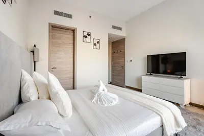a white bedroom with a large bed and a flat screen tv at Luxury Stunning Burj Khalifa View High Floor Big Balcony Pool&Gym 1BR 80m2 in Dubai